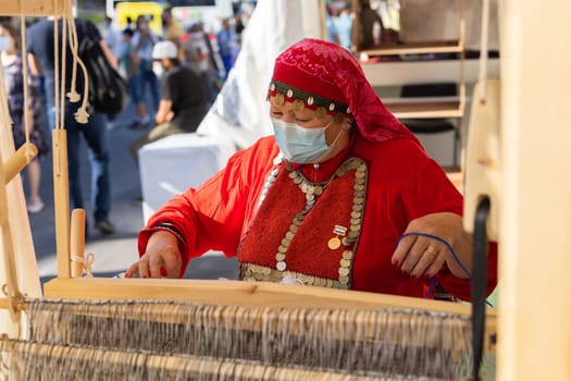 UFA, RUSSIA - JULY 10, 2021: Bashkir woman make carpet during Folkloriada in Ufa