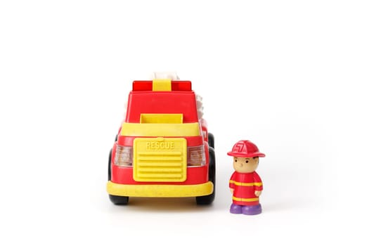 Children's toy red fire truck with a fireman in uniform standing next to him, isolated on whire background.