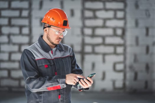 Caucasian male construction worker in overalls using smartphone.