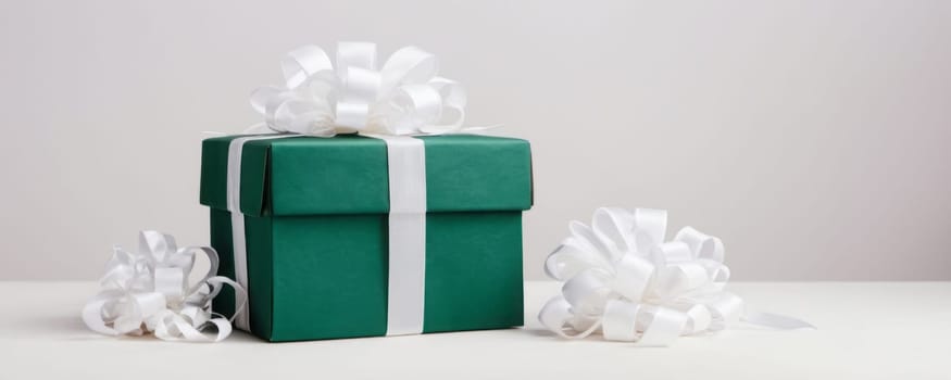 A single green gift box with a white ribbon exudes festive elegance, flanked by loose bows, against a neutral backdrop