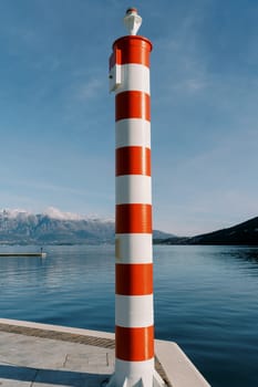 Modern small striped lighthouse with a signal lamp at the top stands on the pier. High quality photo