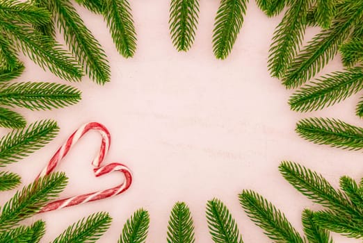 Beautiful Christmas tree branches and heart-shaped Christmas candies lie in a semicircular frame on a pink textured background with copy space in the center, flat lay close-up.