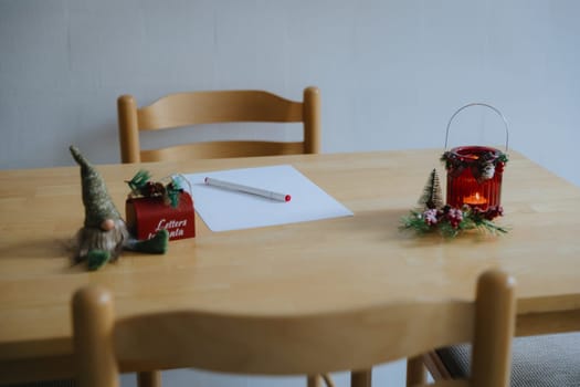 One blank white sheet, a red felt-tip pen and Christmas decor with a burning candle in a jar stand on the table in the dining room on a winter day, side view close-up.