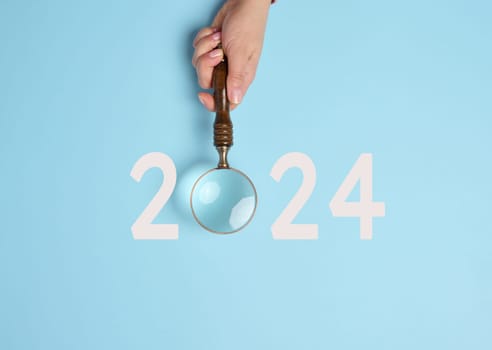 A female hand holds a magnifying glass and the inscription 2024, symbolizing the arrival of the new yea