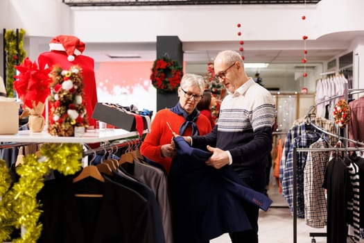 Senior clients looking for jackets on hangers, buying clothes on sale from clothing store at mall. Elderly people checking fashion items, searching formal attire and presents for christmas.