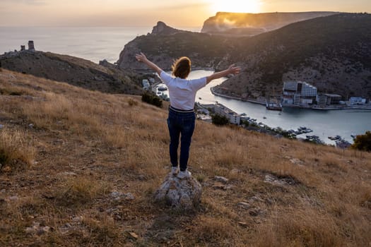 Happy woman on sunset in mountains. Woman standing with her back on the sunset in nature in summer with open hands. Silhouette