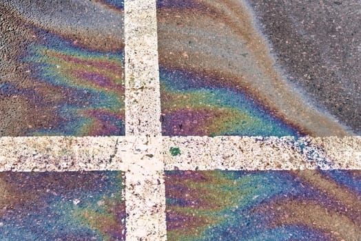 Spill of oil, gasoline or oil on wet asphalt with parking and dividing lines.