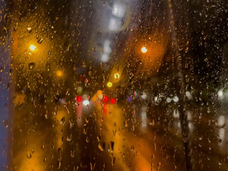 Rain bokeh road lights. Abstract shot of evening city traffic bokeh. Multicolored lights of the evening city and passing cars through a wet rainy window