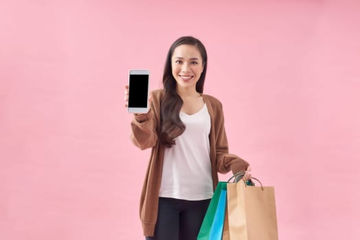 Beautiful Attractive Asian Woman holding shopping bags and showing mobile phone screen on pink
