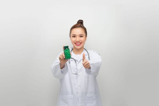 Portrait of happy woman doctor shows green medicine bottle and thumb up
