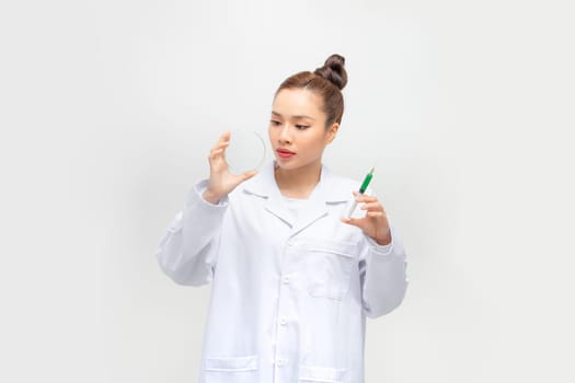 Young female doctor looking at liquid sample in  petri dish on isolated background