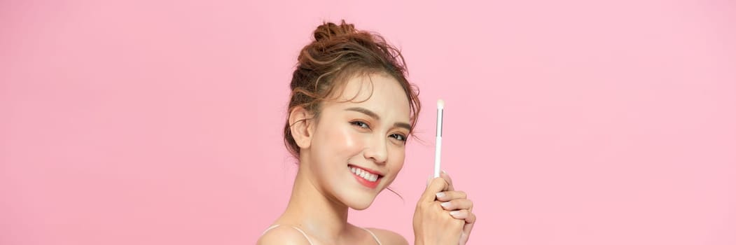 a young woman holding brush in her hand and applying makeup