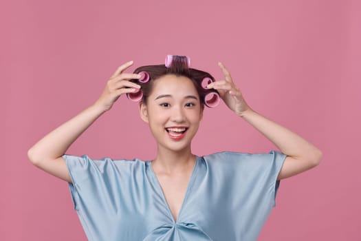 Cheerful asian girl with hair curlers rollers by hairdresser.