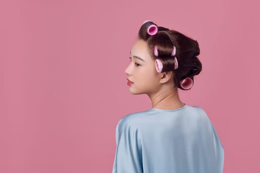 Seductive young lady in hair rollers posing and looking away on white background