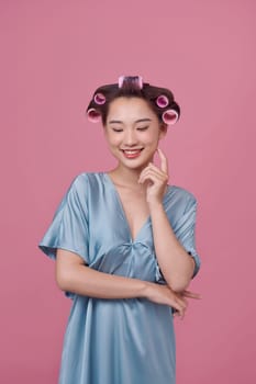 Cheerful young model posing with hair curlers on pink background