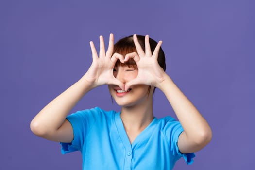 Young beautiful asian woman doing heart shape with hand and fingers smiling looking through sign