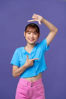 Beautiful young woman looking at camera and gesturing finger frame while standing against purple background