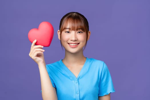 Smiling woman holding red heart on purple background