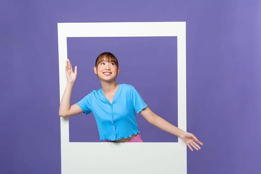 Portrait of lovely funny cheerful girl in big photo frame isolated over purple background