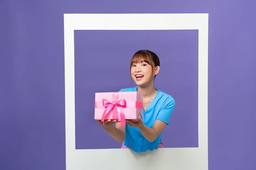 Photo of funny excited young woman holding giftbox inside white photo frame over color background