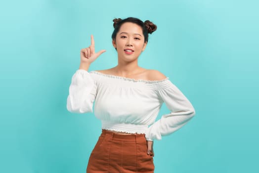 Young woman over blue background smiling and  pointing with two hands and fingers to top side.