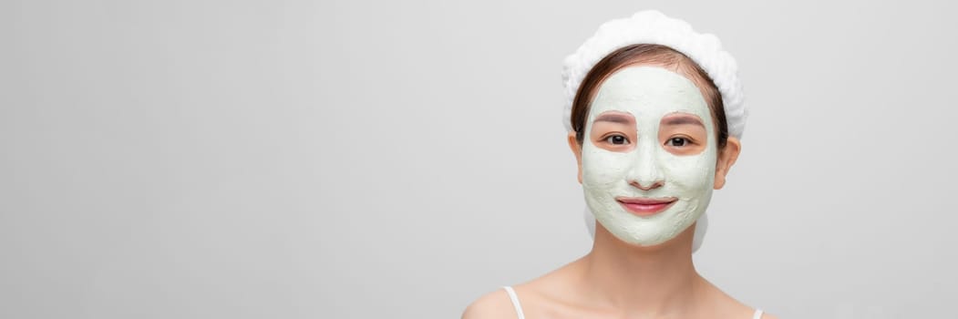 Beautiful young woman with clay facial mask, beauty treatment over white banner