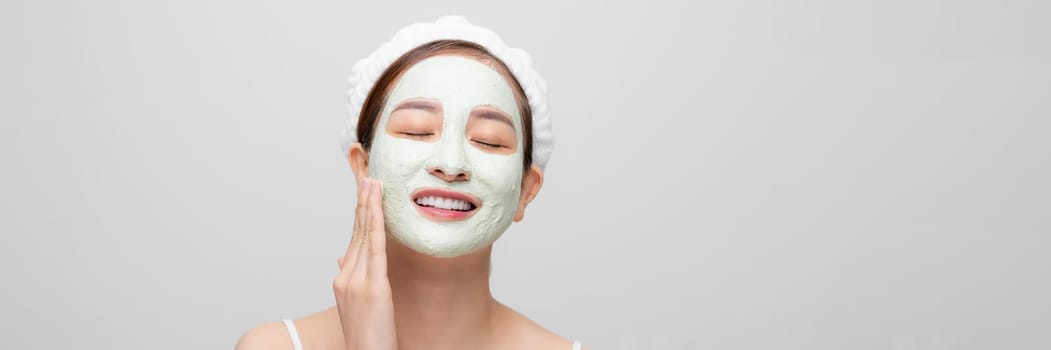 Beautiful woman is getting facial clay mask on white banner background.