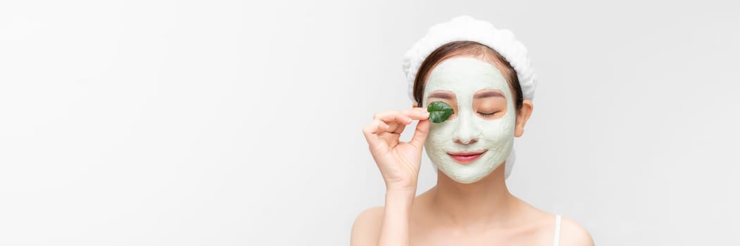 Young girl enjoys clay facial mask posing with a leaf on white banner.