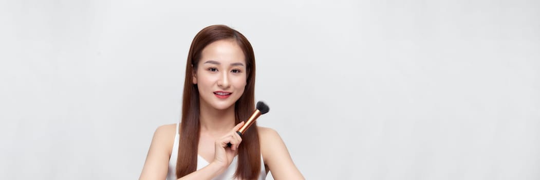Banner of beautiful young woman holding makeup brush isolated over white background