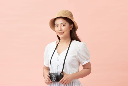 A smiling young woman in summer hat standing with photo camera isolated over pink background