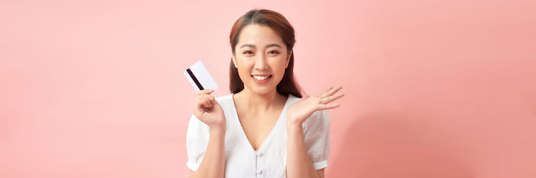 Happy young Asian woman showing credit card with open palm gesture isolated on banner background 