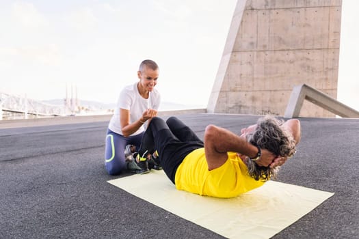 female personal trainer assisting a senior sports man with abs workout, concept of active and healthy lifestyle in middle age