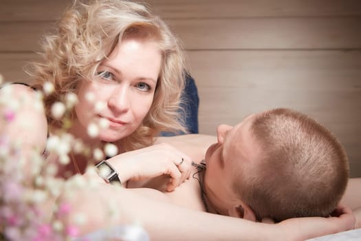 Loving enamored adult couple communicates, embraces, and has fun alone together on the bed in the bedroom or hotel room. The woman is wearing tank top and the man is shirtless