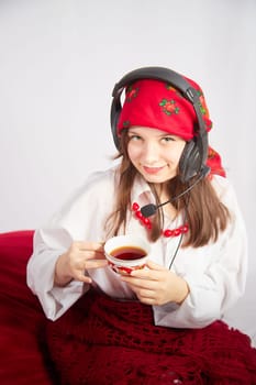 Portrait of young girl in a bright red scarf and large headphones with a microphone. A woman who is radio or television presenter with cap of tee. Funny female telecom operator. Freelancer at work