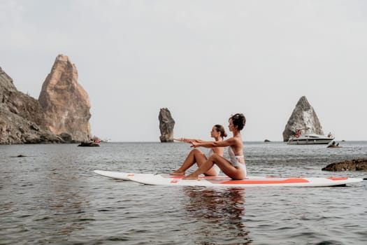 Woman sup yoga. Middle age sporty woman practising yoga pilates on paddle sup surfboard. Female stretching doing workout on sea water. Modern individual hipster outdoor summer sport activity