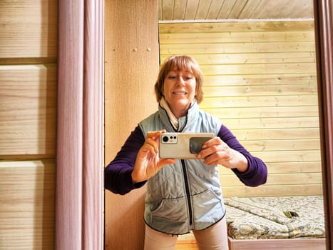 Middle-aged woman using smartphone for selfie and blogging. Female blogger poses in a photo. The girl admires herself in the mirror