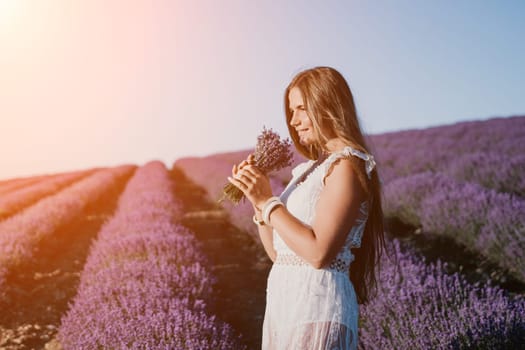 Close up portrait of young beautiful woman in a white dress and a hat is walking in the lavender field and smelling lavender bouquet.