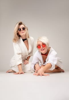 two girls in white coats and glasses are having fun with emotions sitting in the studio on a white background of a copy paste