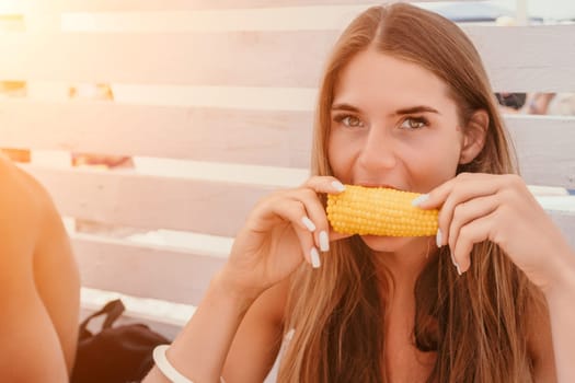 Healthy vegetarian hipster woman in summer outfit eat grilled corn and look to camera. Sexy lady on sea beach sunset or ocean sunrise. Travel, explore, active yoga and meditation lifestyle concept.