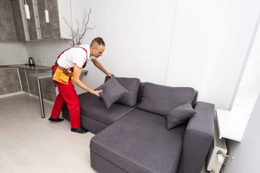 Loader moves sofa, couch. worker in overalls lifts up sofa, white background. Delivery service concept. Courier delivers furniture in case of move out, relocation. High quality photo