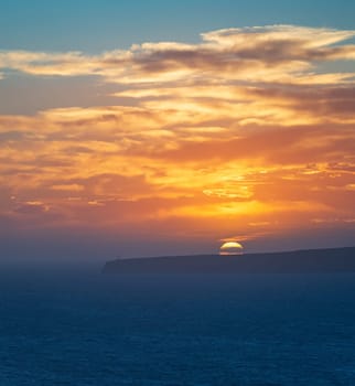 Spectacular sunset with clouds over cliffs and ocean, capped by a sentinel lighthouse.