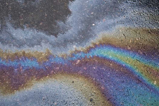 Abstract colored background of leaked gasoline on wet asphalt close-up.