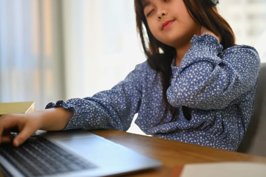 Exhausted schooler girl suffering from doing homework or studying online on laptop at home