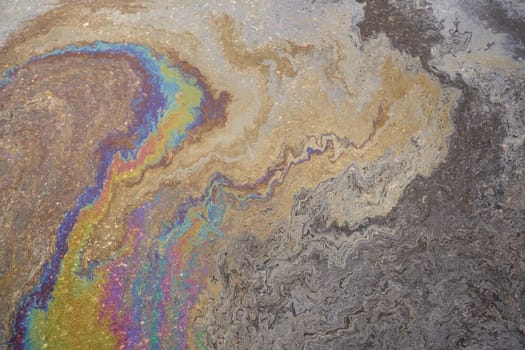 Close-up of an iridescent oil or gasoline spill on a wet asphalt, viewed from above. Bold multicolored spots on the asphalt. Concept of environmental problems