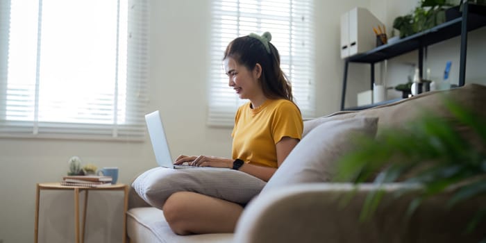 Young woman Asian using laptop pc computer on couch relax surfing the internet at home. lifestyle relaxation concept.