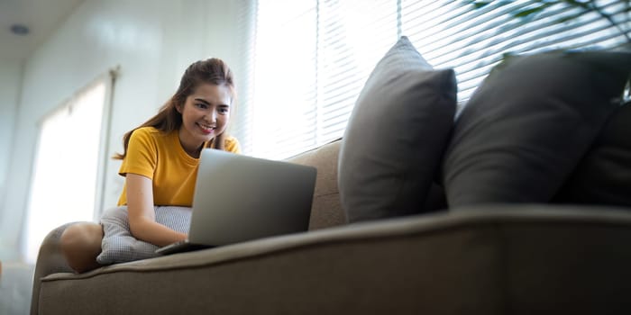 Young woman Asian using laptop pc computer on couch relax surfing the internet at home. lifestyle relaxation concept.