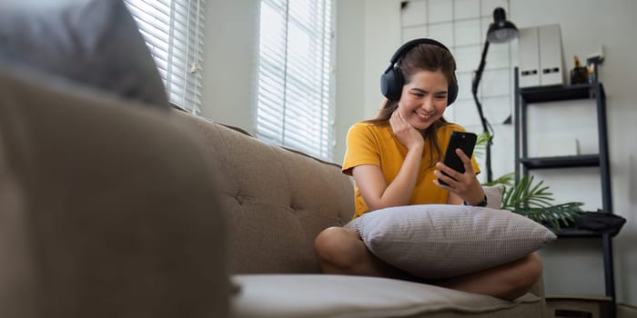 Asian beautiful woman smile at home in headphones. young woman listen music on smartphone at home. Use technology, lifestyle relaxation concept.