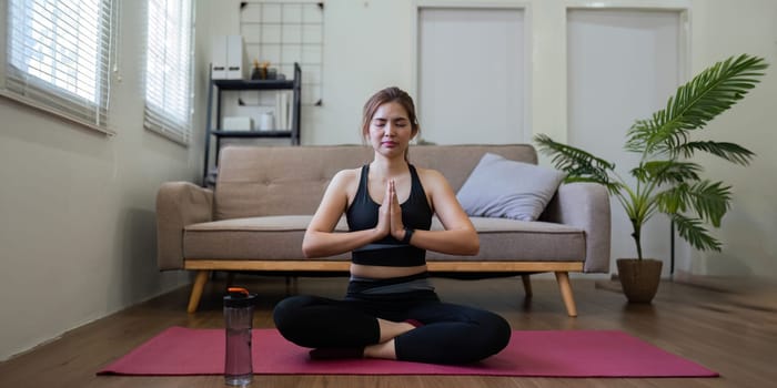 Young Asian woman meditating with trainer online at home.