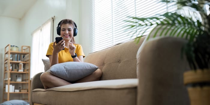 Asian beautiful woman smile at home in headphones. young woman listen music on smartphone at home. Use technology, lifestyle relaxation concept.