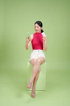 Smiling young woman using mobile phone and holding credit card isolated over green
